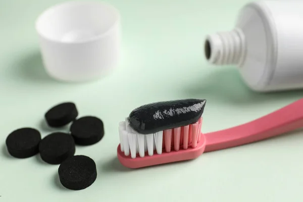 Brush with charcoal toothpaste and tablets on white background, closeup