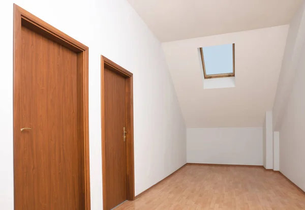 Light spacious attic room with doors and window on slanted ceiling