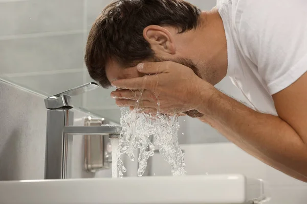 Handsome man washing face in bathroom, closeup