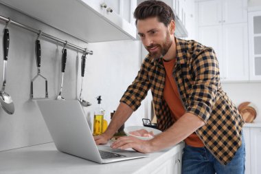 Adam mutfakta dizüstü bilgisayarla yemek pişirirken yemek yapıyor.