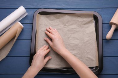 Mavi ahşap masanın tepsisine parşömen kağıdı koyan kadın.