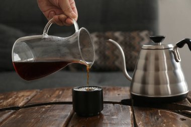 Kafedeki ahşap masada fincana kahve dolduran barista, yakın plan.