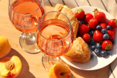 Glasses of delicious rose wine and food on wooden board, closeup