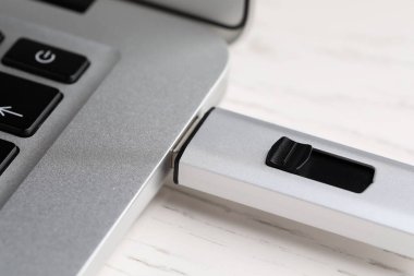 Modern USB flaş bellek beyaz tahta masadaki dizüstü bilgisayara bağlı, yakın plan.