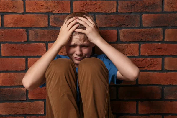 レンガの壁の近くに座って動揺した少年 子供のいじめ — ストック写真