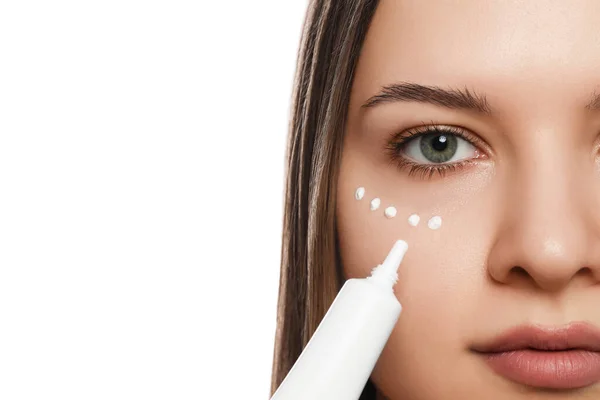 Mujer Joven Aplicando Crema Bajo Los Ojos Sobre Fondo Blanco —  Fotos de Stock