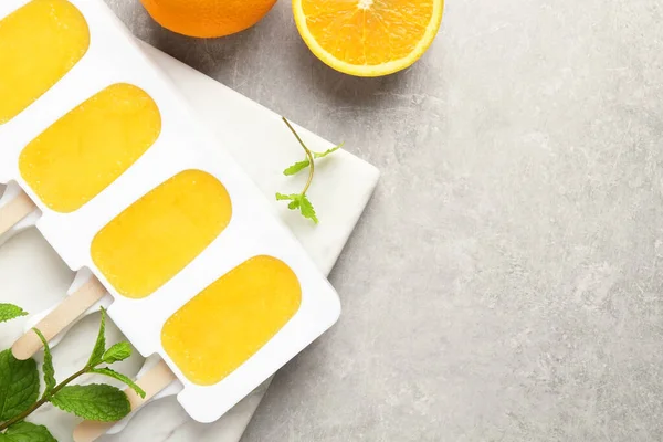 Tasty orange ice pops in mold and space for text on light grey table, flat lay. Fruit popsicle