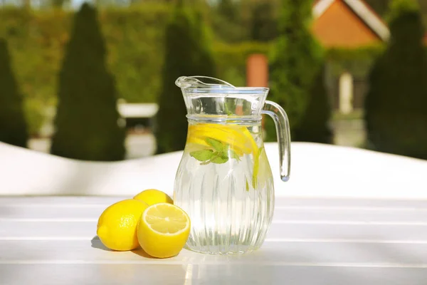 Jug of water with lemons and mint on white wooden table outdoors
