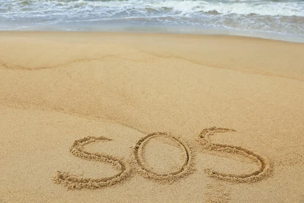 stock image Message SOS drawn on sand near sea