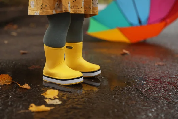 小さな女の子は黄色のゴム製のブーツを着て屋外の水たまりの中に立って クローズアップ — ストック写真