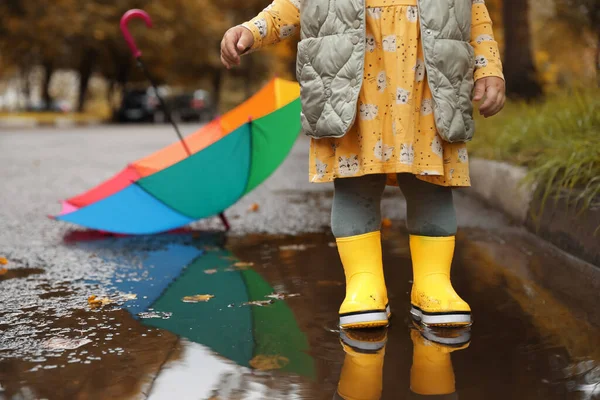 小さな女の子は黄色のゴム製のブーツを屋外の水たまりの中に立って着て 閉じます テキストのスペース — ストック写真