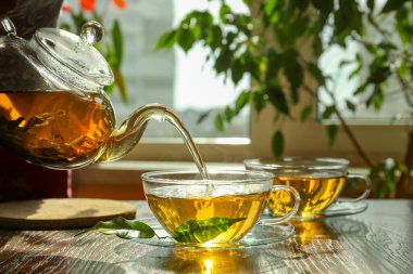 Yeşil çayı çay bardağına çay tabağı ve ahşap masa yapraklarıyla dolduruyorum.