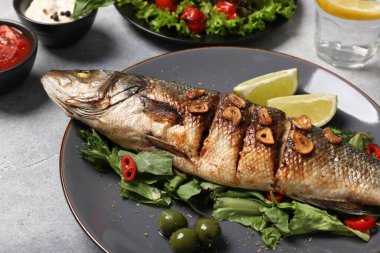 Lezzetli levrek balığı ve malzemeleri açık gri masada, yakın plan.