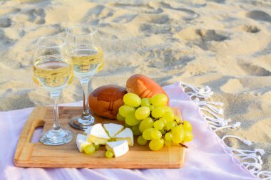 Glasses with white wine and snacks on beach sand outdoors. Space for text clipart