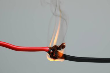 Gri arkaplanda iltihaplı kırmızı kablo, yakın plan. Elektrik kısa devresi