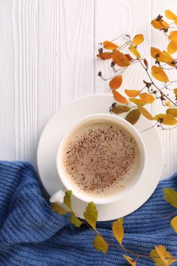 Bir fincan sıcak içecek, yapraklar ve beyaz ahşap masaya örülmüş süveter, düz yatış. Sıcak sonbahar atmosferi