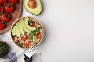 Domatesli nefis kinoa salatası, avokado dilimleri ve beyaz masada servis edilen ıspanak yaprakları. Metin için boşluk