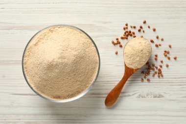 Beyaz ahşap masa üzerinde karabuğday unlu kase ve kaşık, düz.