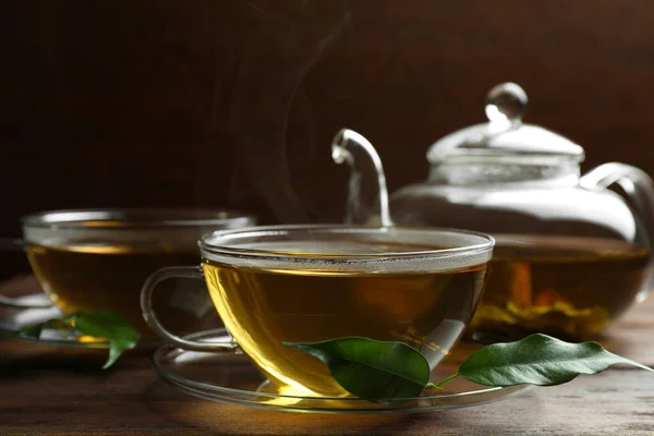 玻璃杯中的新鲜绿茶 木制桌子上的叶子和茶壶 — 图库照片