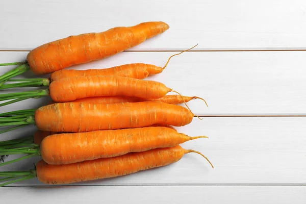 Many tasty ripe carrots on white wooden table, flat lay. Space for text