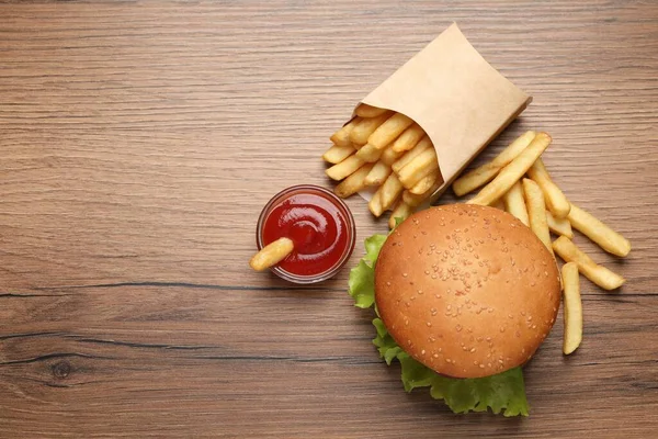 French fries, tasty burger and sauce on wooden table, flat lay. Space for text