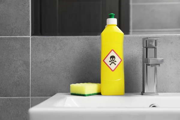 Bottle of toxic household chemical with warning sign and scouring sponge in bathroom, space for text