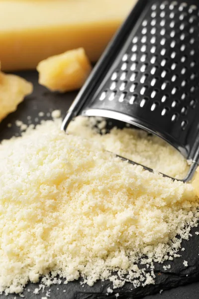 Pile of grated parmesan cheese and grater on black table, closeup