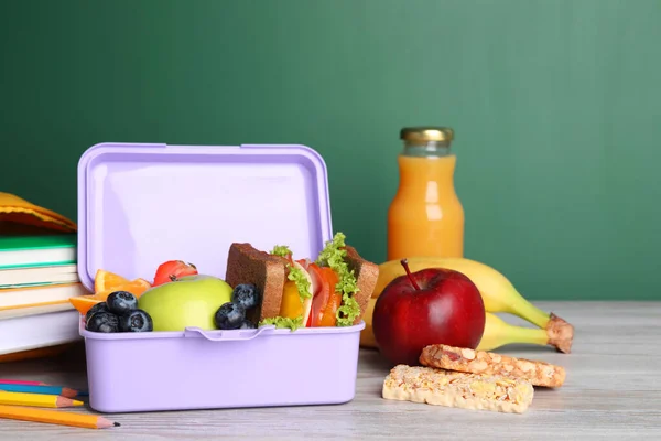 健康的な食べ物と緑の黒板の近くの軽い木製のテーブルの上のさまざまな文房具と弁当箱 — ストック写真