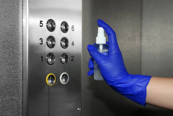 Woman cleaning buttons panel in elevator with detergent spray, closeup