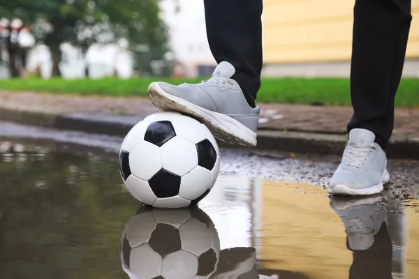 Man with soccer ball near puddle outdoors, closeup