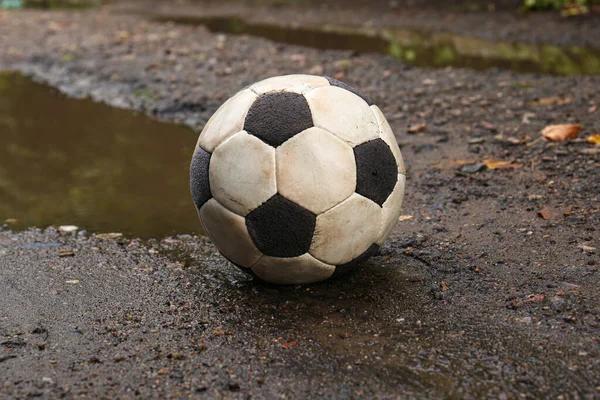 Dirty soccer ball near puddle on ground