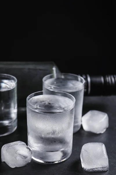 ウォッカのボトルと黒を背景にテーブルの上に氷とショットグラス — ストック写真