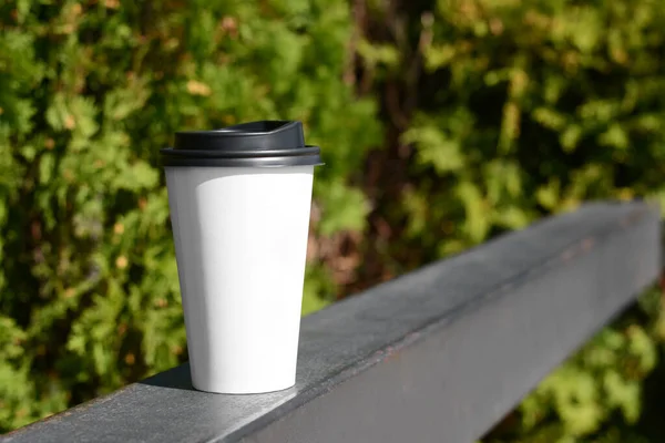 Takeaway coffee cup on metal railing outdoors. Space for text