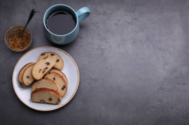 Kuru üzümlü tatlı krakerler, reçel ve bir fincan çay, gri masa, düz yatış. Metin için boşluk