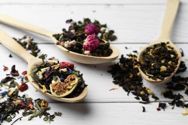 Kurutulmuş çay yapraklı kaşıklar ve beyaz ahşap masada meyveler, yakın plan.