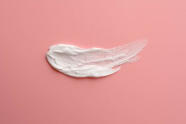 Pembe arka planda yüz kremi örneği, üst görünümde.
