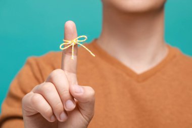 Man showing index finger with tied bow as reminder against turquoise background, focus on hand clipart