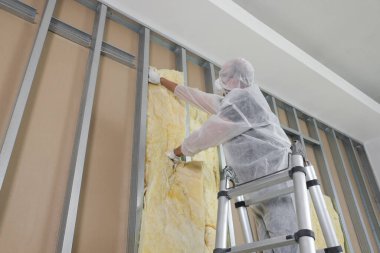 Kapalı alanda merdiven kullanarak duvarı yalıtan işçiler, düşük açılı görüş.