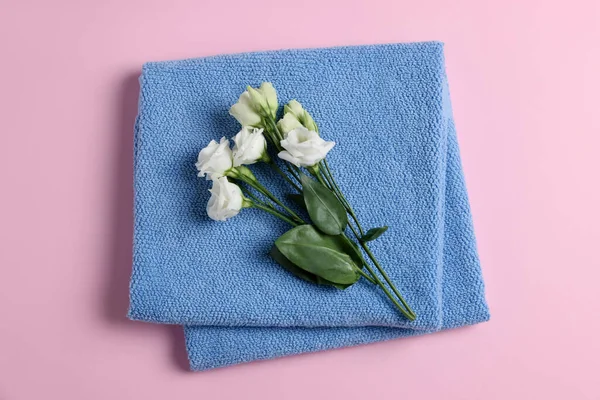 Soft folded blue towel with flowers on pink background, top view