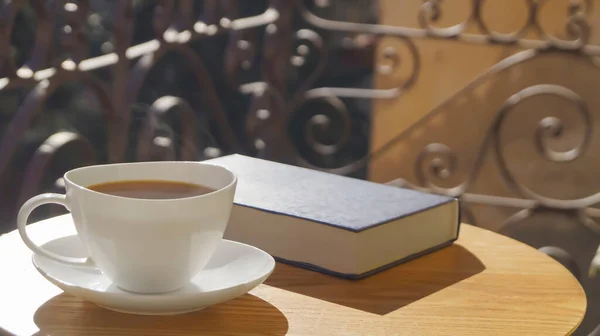 Cup of aromatic coffee and book on wooden table outdoors, space for text