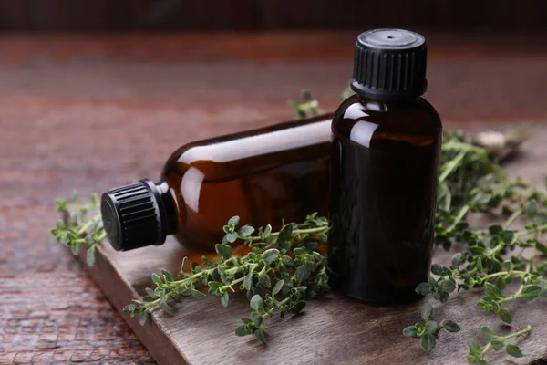 Bottles of thyme essential oil and fresh plant on wooden table, closeup
