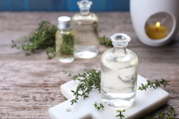 Thyme essential oil and fresh plant on wooden table, space for text