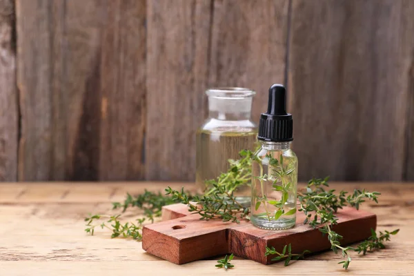 Bottles of thyme essential oil and fresh plant on wooden table, space for text