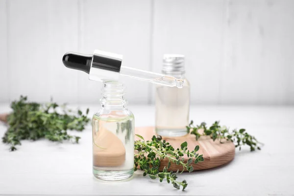Thyme essential oil and fresh plant on white wooden table