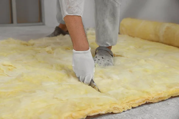 Worker in gloves cutting insulation material indoors, closeup