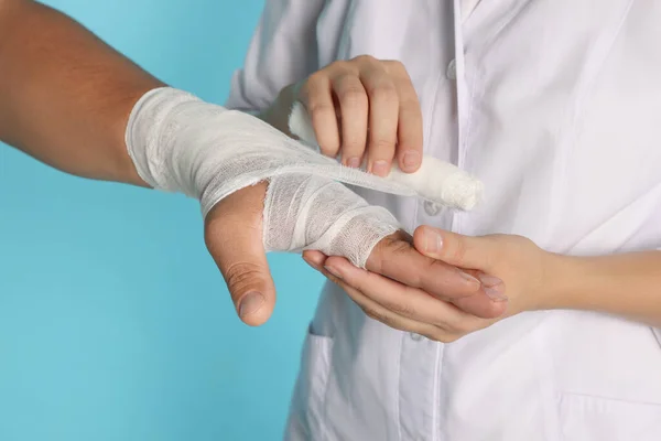 薄い青の背景に患者の手に包帯を適用する医師 クローズアップ — ストック写真