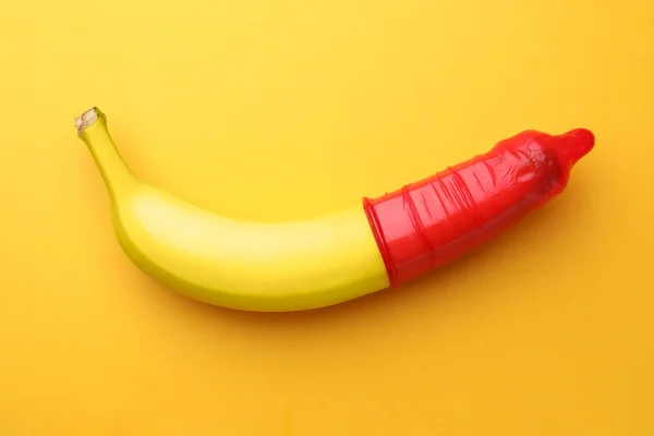 stock image Banana with condom on orange background, top view. Safe sex concept