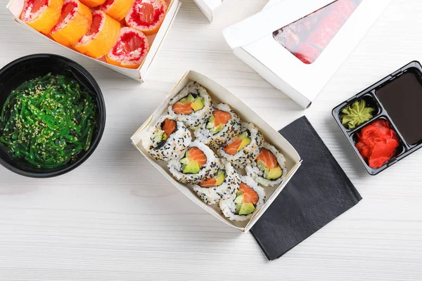 食料の配達だ 白い木のテーブルの上においしい寿司ロールを持つ紙箱 — ストック写真