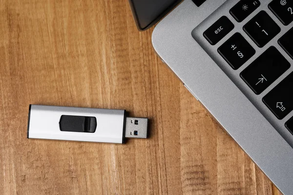 Stock image Modern laptop and usb flash drive on wooden table, flat lay