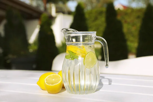 Jug of water with lemons and mint on white wooden table outdoors